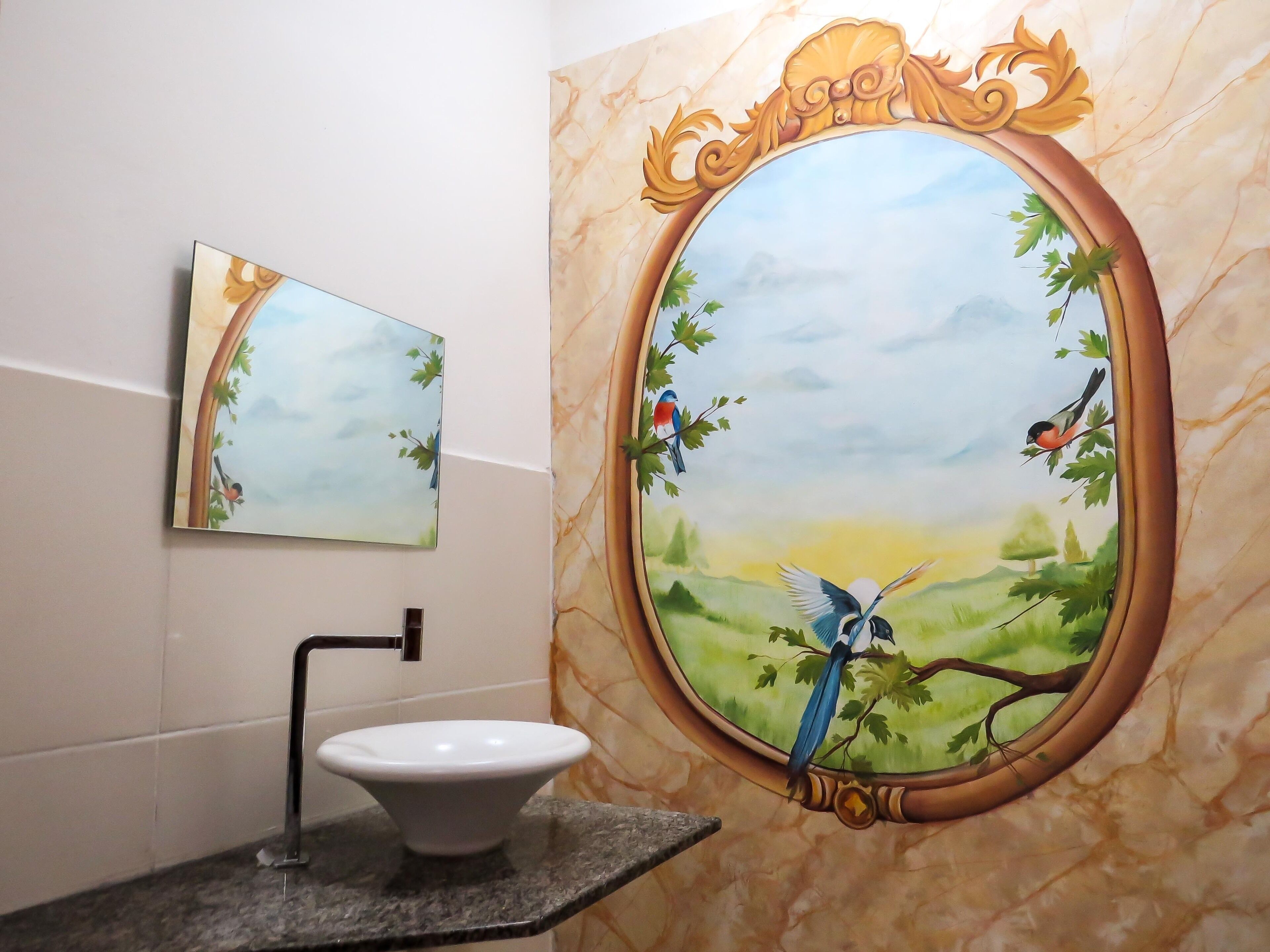 A bathroom with a marble wall, a sink, and a mirror framed with a bird painting.
