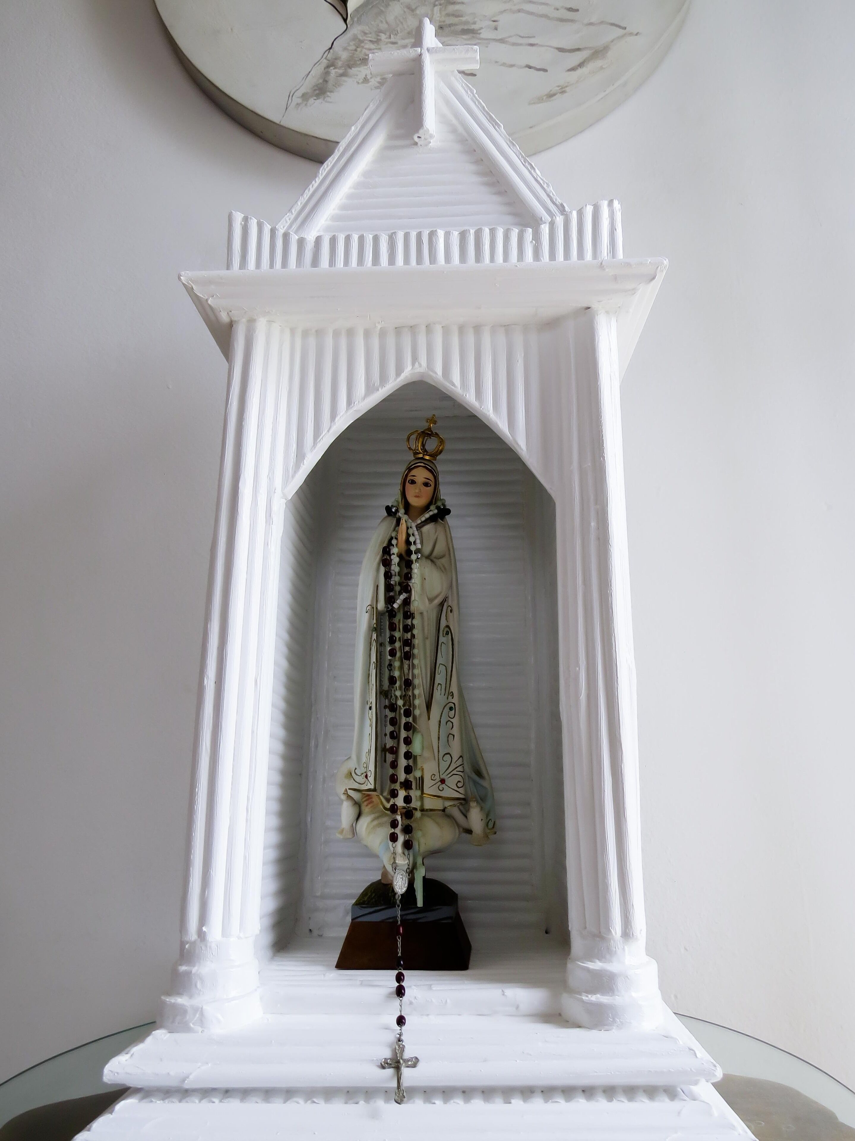 A white religious statue in a niche with a cross base.