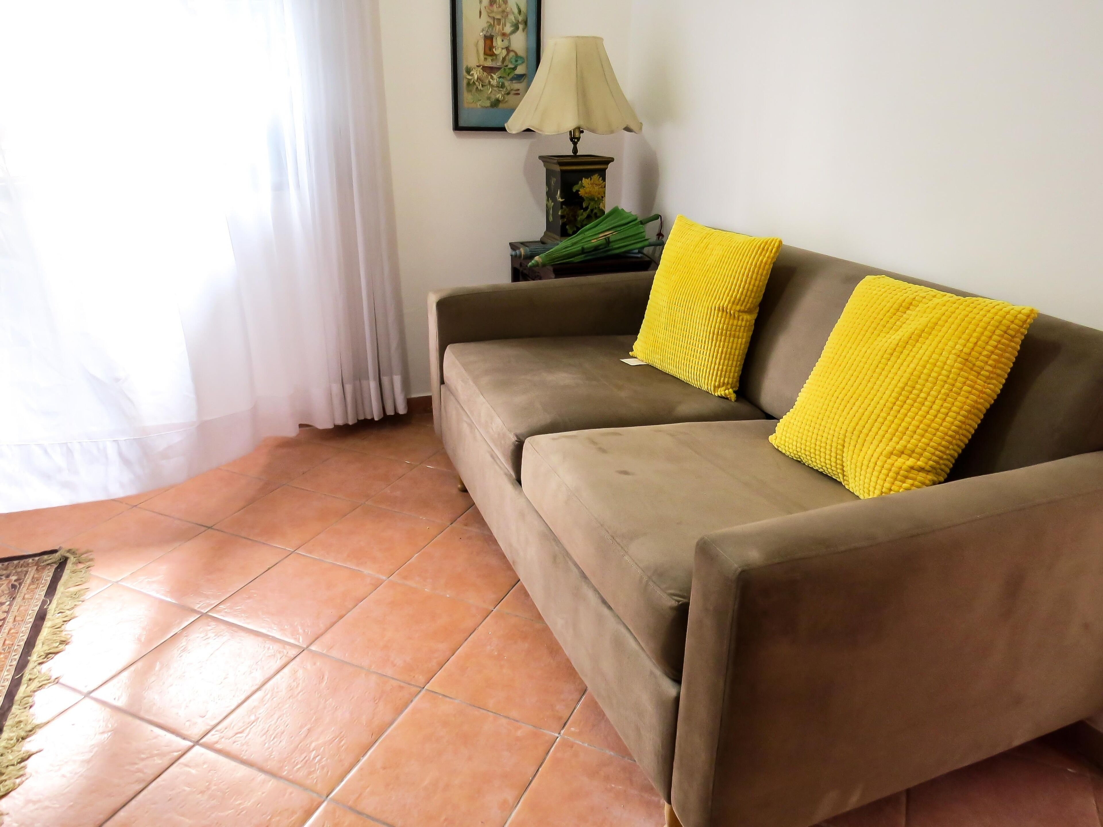 A living room with a brown sofa, two yellow cushions, a lamp, and a painting on the wall.