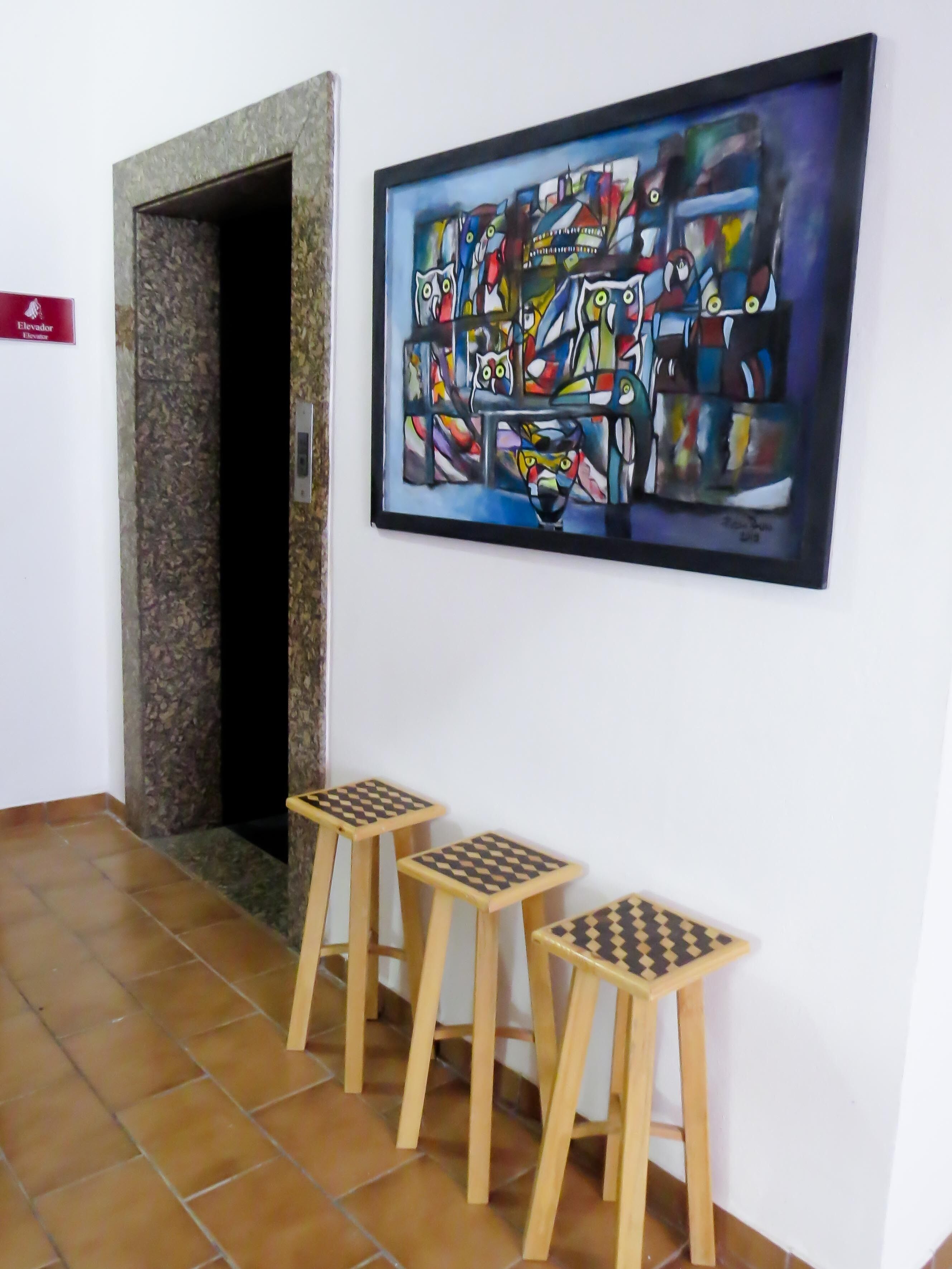 A hallway with a tiled floor, a door, and a framed abstract painting on the wall.