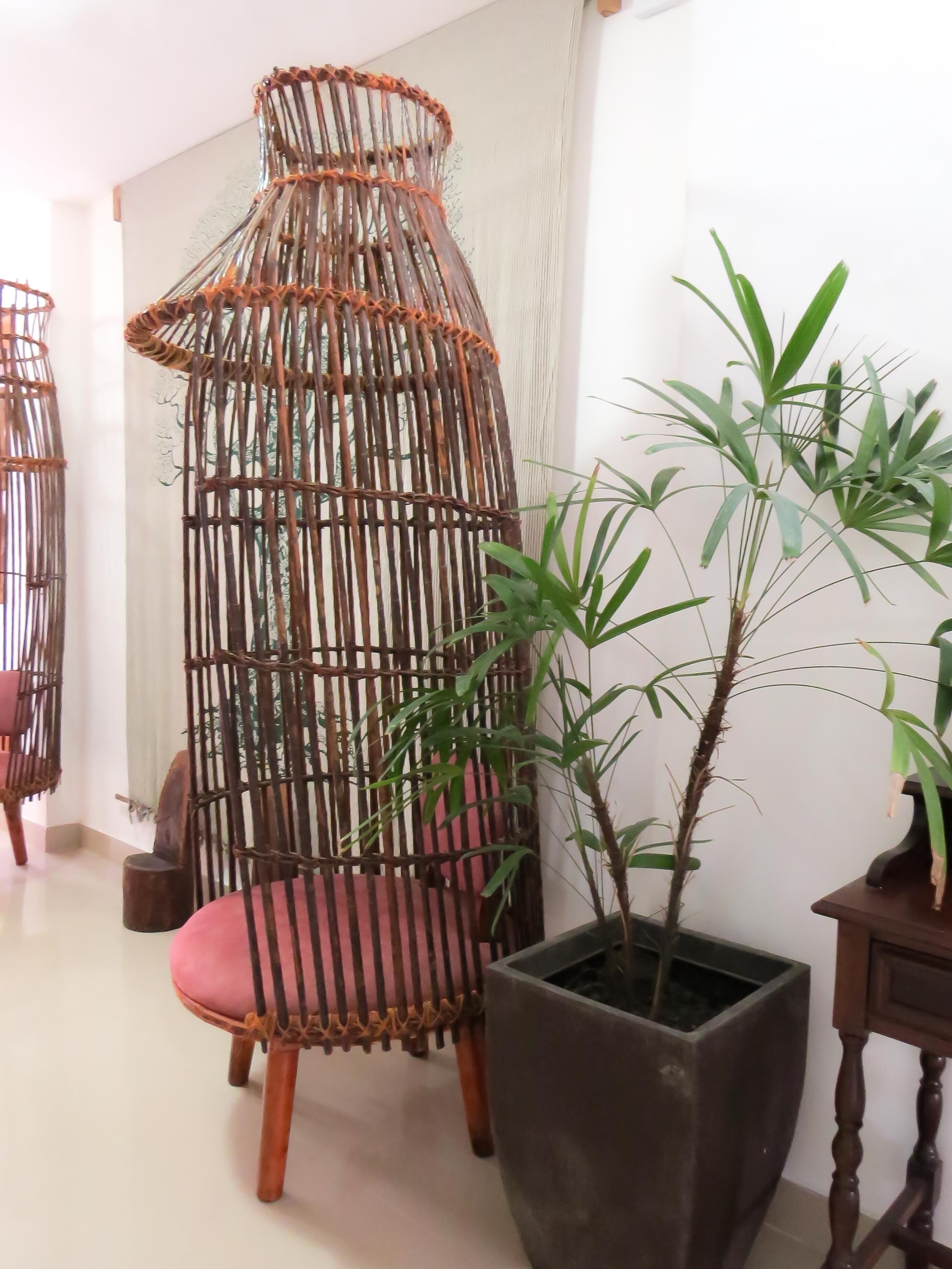A room with a hanging chair made of bamboo, a potted bamboo plant, and a wooden table.