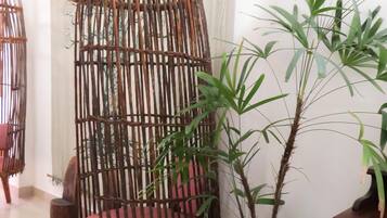 A room with a hanging chair made of bamboo, a potted bamboo plant, and a wooden table.