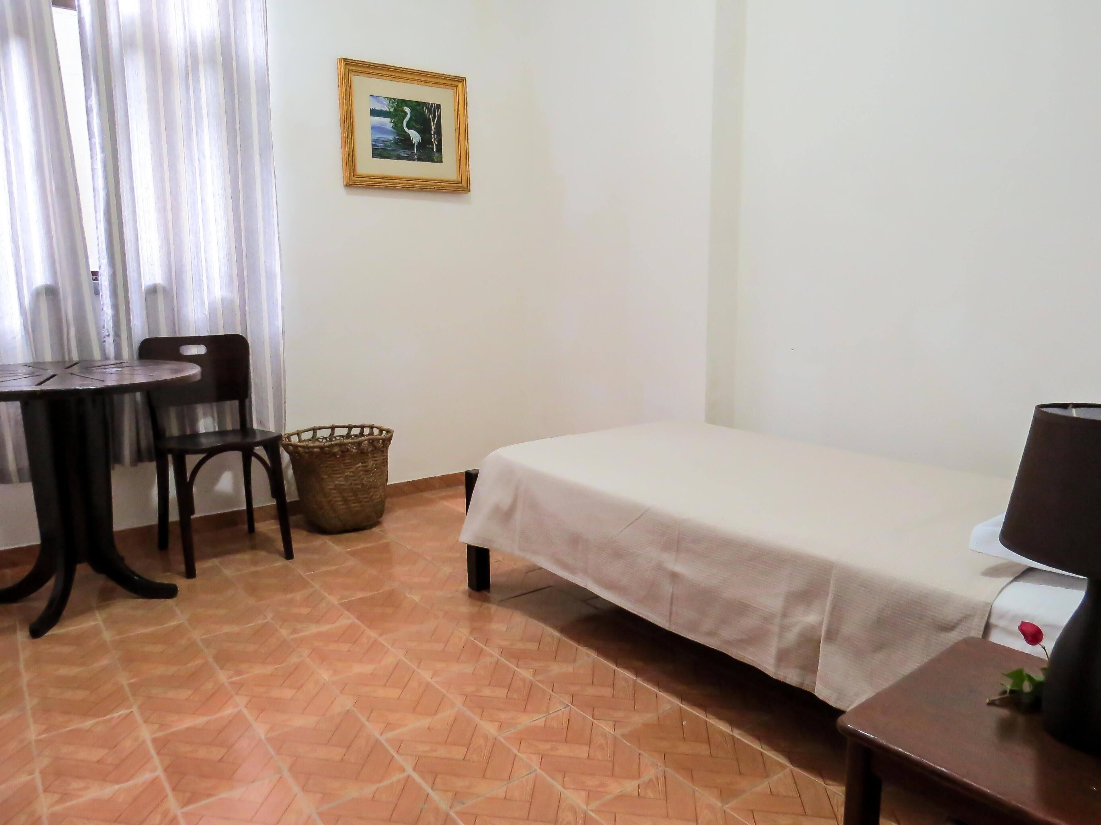 Una habitación con una cama, una mesa con sillas, un televisor y un cuadro en la pared.