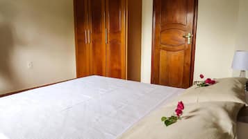 A hotel room with a bed, wooden wardrobe, and a nightstand with a lamp and a rose.