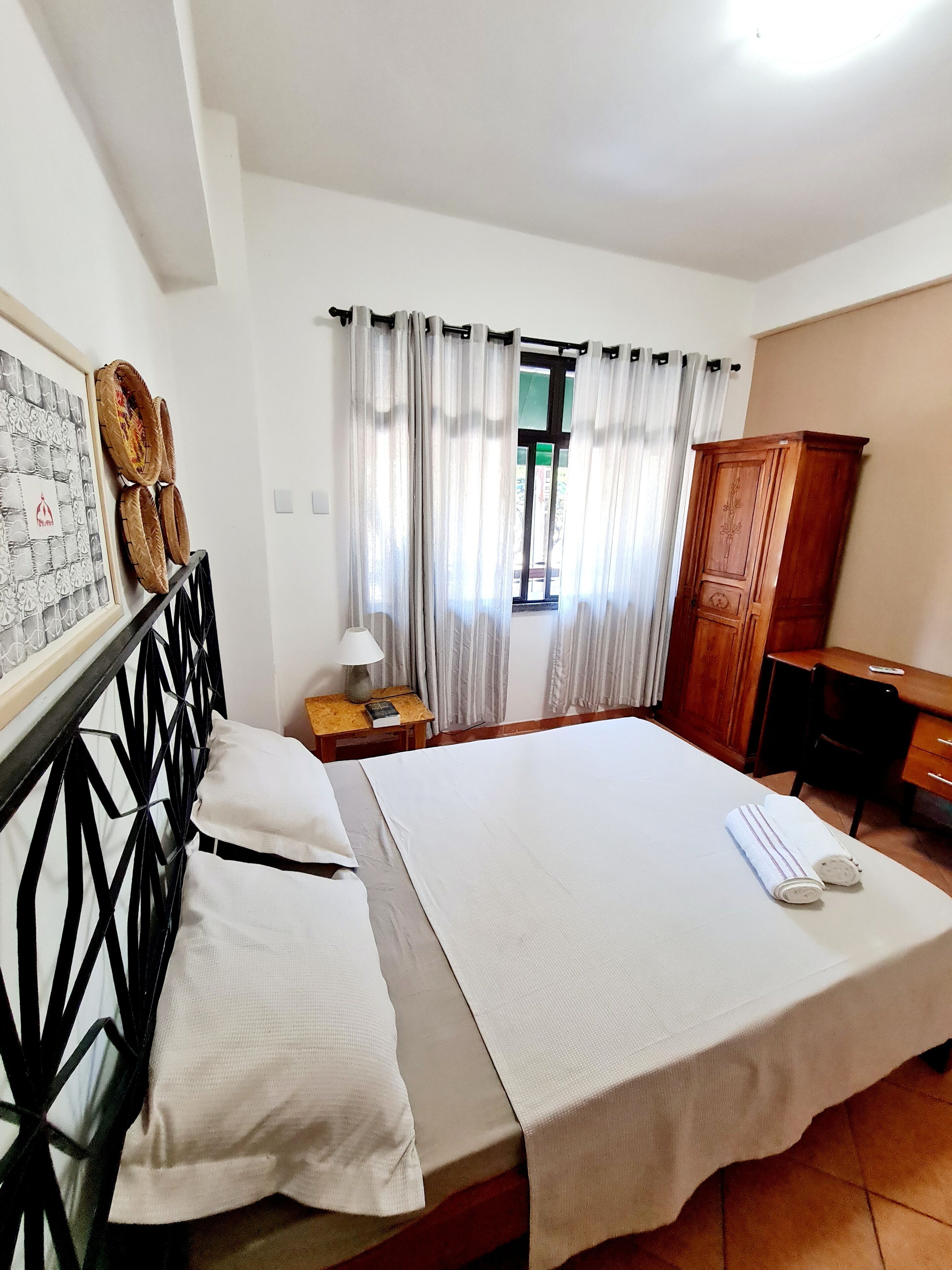 A hotel room with a bed, a desk, a wardrobe, and a window with curtains.