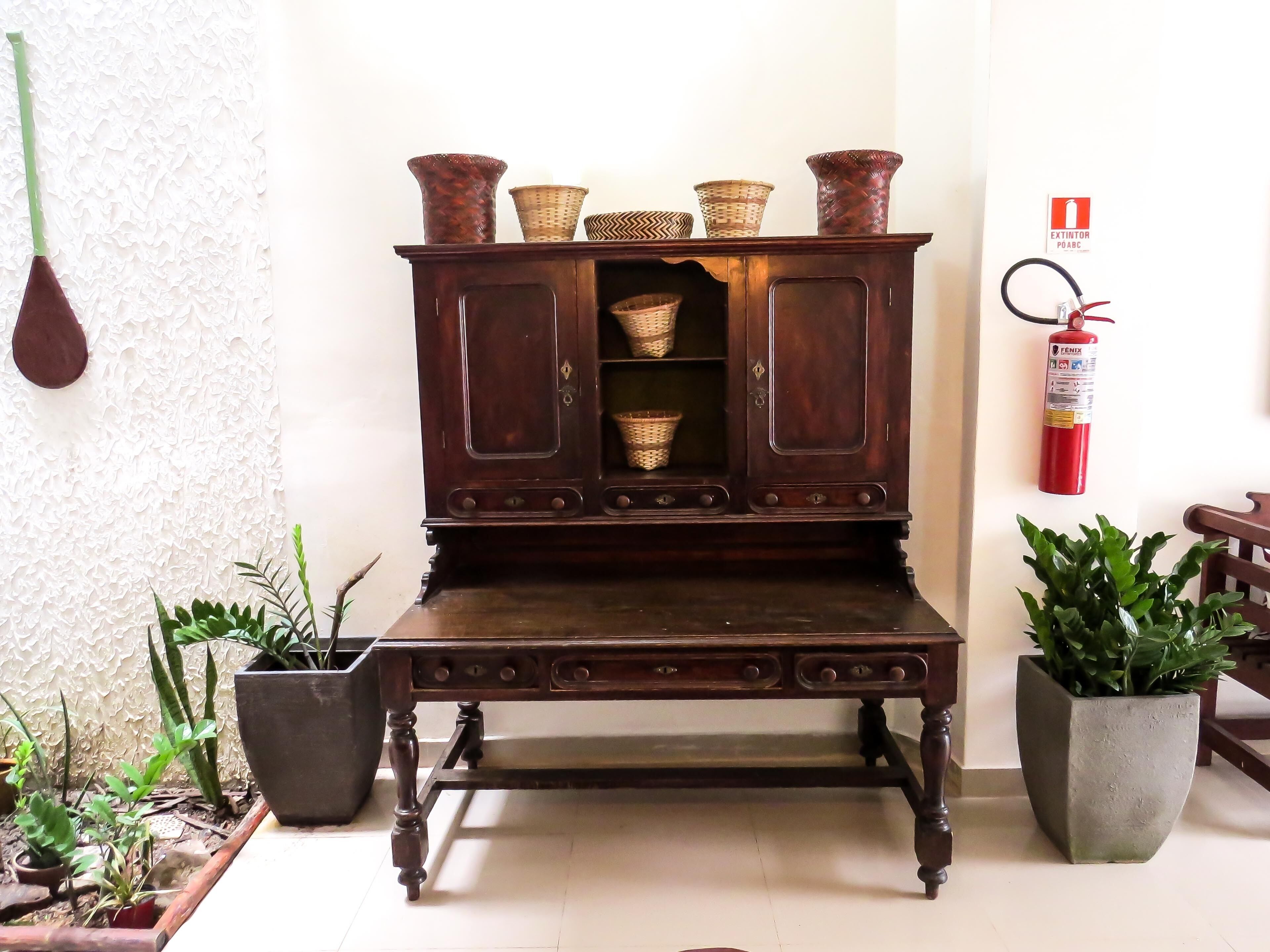 A wooden cabinet with baskets, a fire extinguisher, and potted plants.