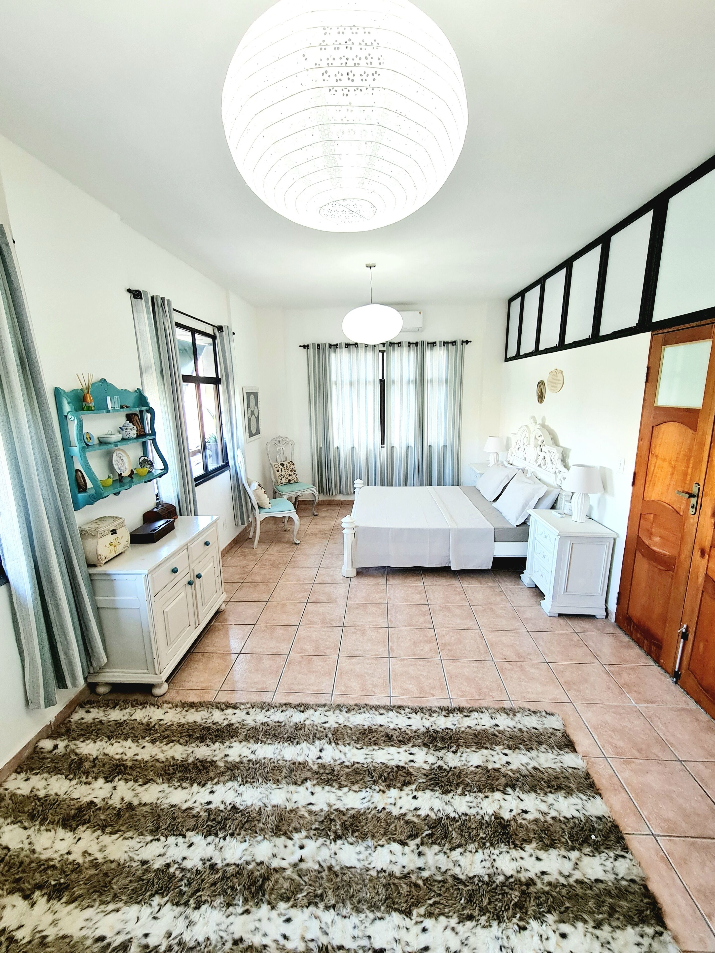 A bedroom with a bed, bedside tables, a dresser, and a large window with curtains.