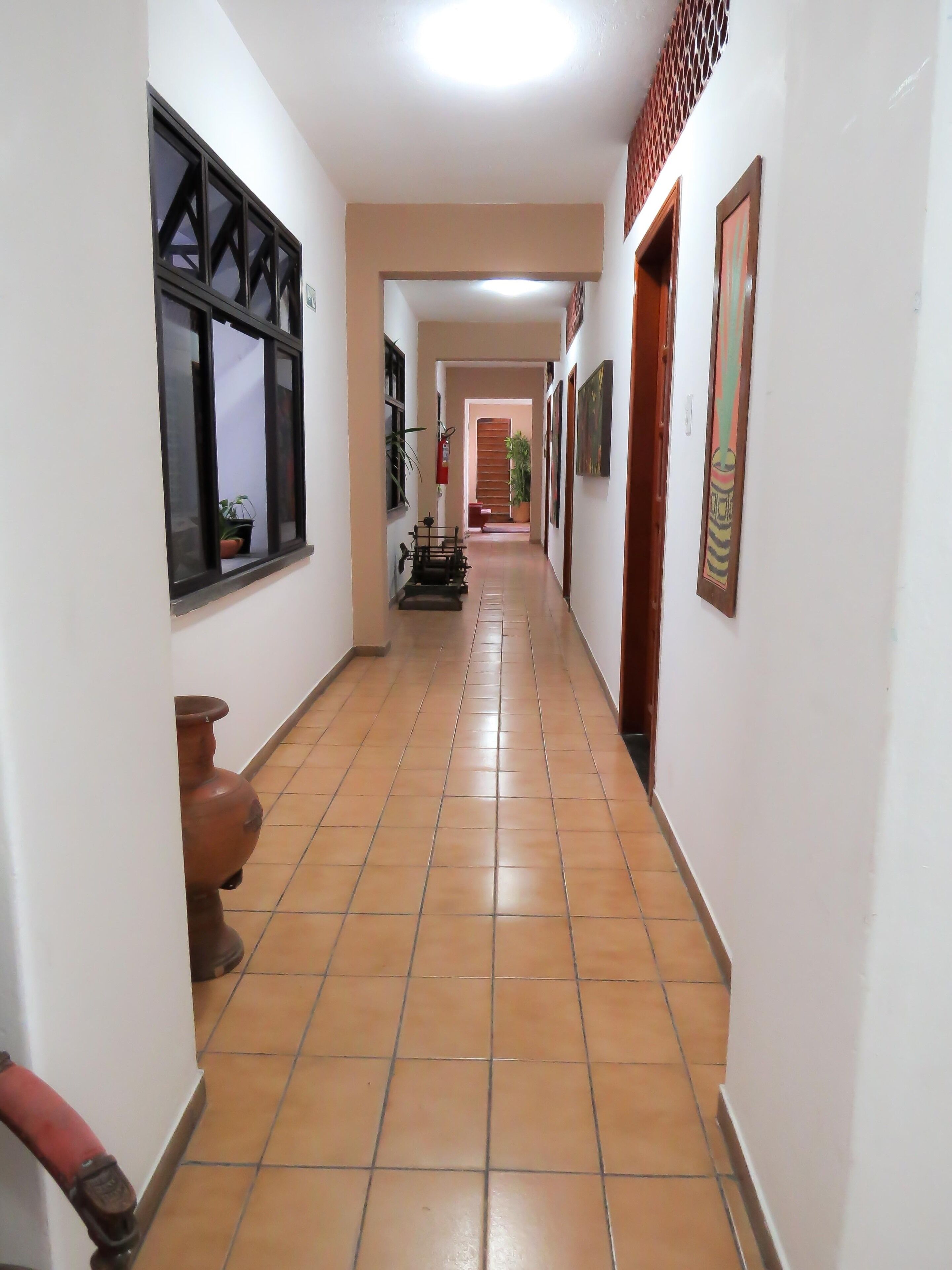 A hallway with tiled flooring, a potted plant, a fire extinguisher, and a door at the end.
