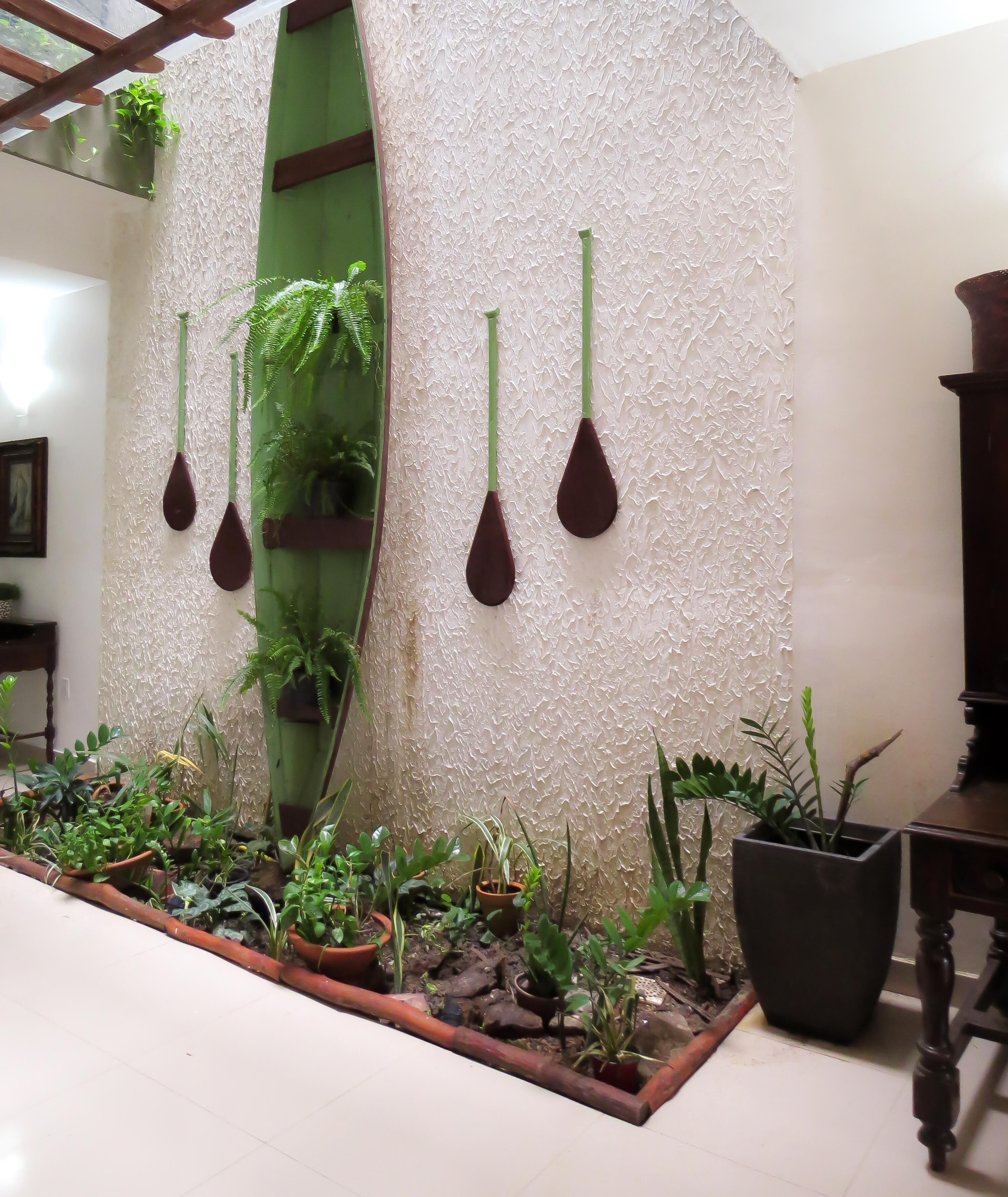 A room with a textured wall, a green plant shelf, hanging planters, and a variety of potted plants on the floor.