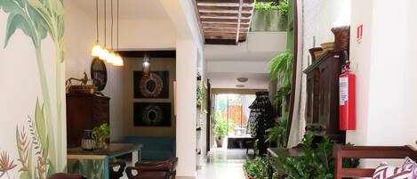 A spacious living area with a dining table, chairs, a sofa, and a bench. There are potted plants and a fire extinguisher on the wall.