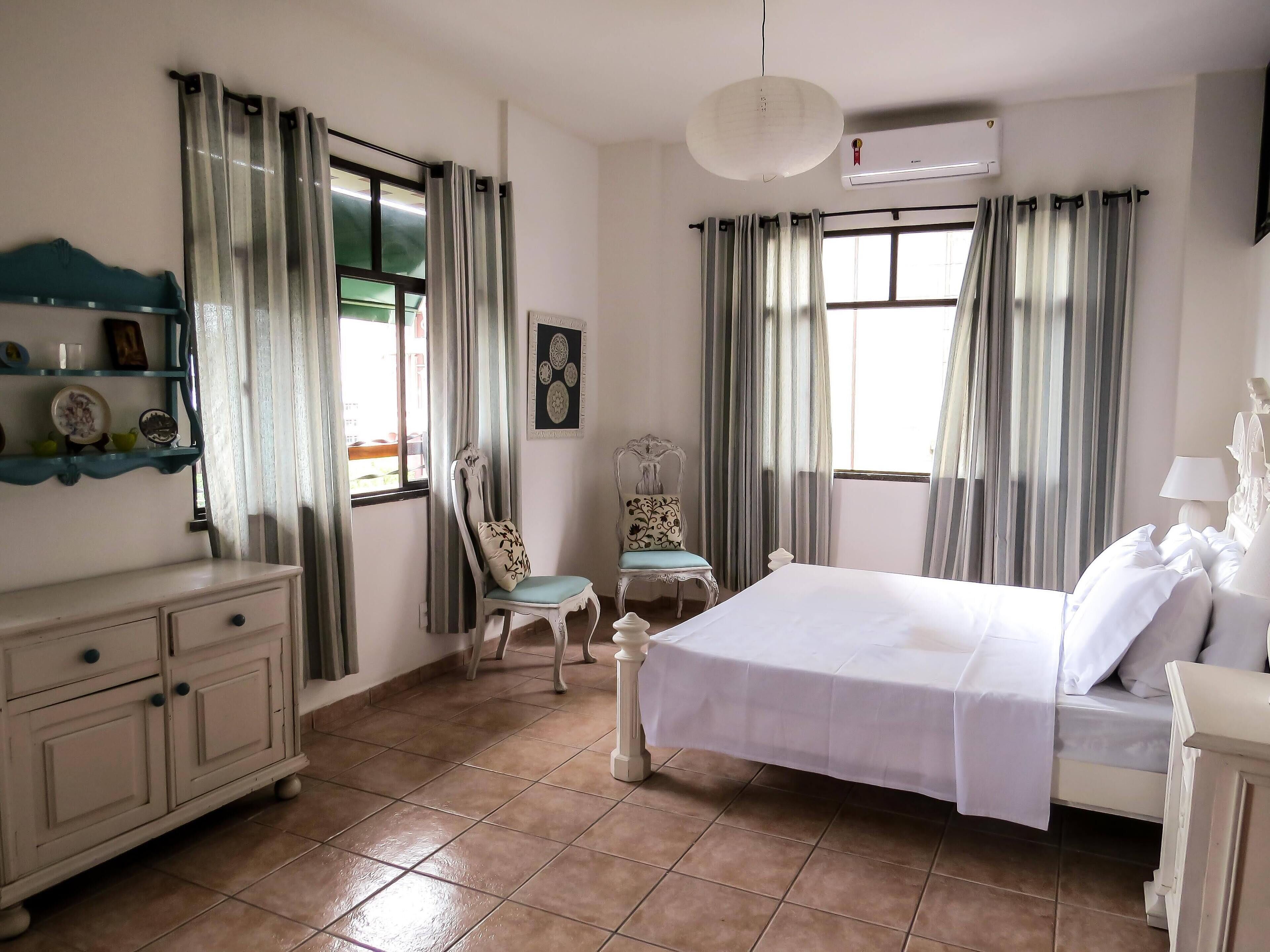 A hotel room with a bed, a chair, a dresser, and a window with curtains.