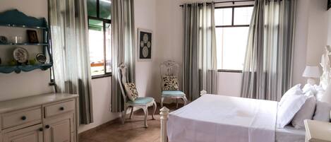 Ein Hotelzimmer mit Bett, Sessel, Kommode und einem Fenster mit Vorhängen.