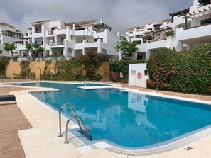 A swimming pool with a metal ladder, surrounded by white buildings with balconies and a hedge. - Quiet apartment perfect for the Family, 4 swimming pools, close to the beach (Alcaidesa)
