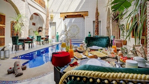 Un espace piscine intérieur luxueux, aménagé avec un coin repas comprenant une table où sont disposés des aliments pour le petit-déjeuner et une chaise placée au bord de la piscine.