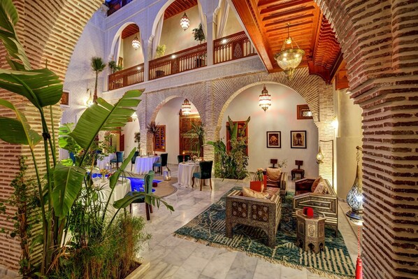 A spacious lobby with high ceilings, arched brick columns, and a central seating area with a patterned rug. - Riad Janate & SPA - Suite Familiale (Marrakech)