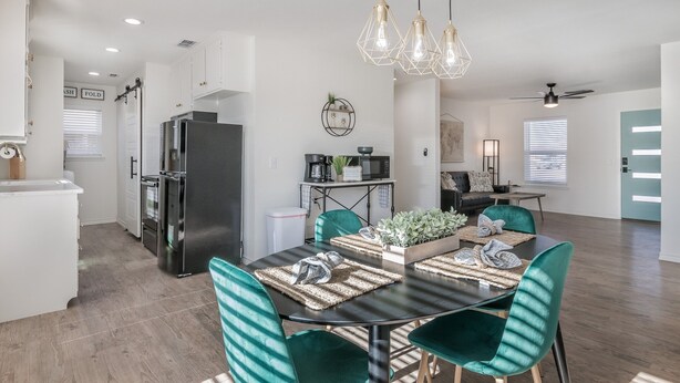A modern kitchen with a black refrigerator, white cabinets, and a dining area with green chairs and a black table. - 18th Street Retreat  (Dumas)