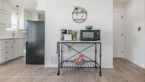 A modern kitchen with white cabinets, a black refrigerator, a microwave, and a small table with a basket. - 18th Street Retreat  (Dumas)