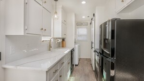 A modern kitchen with white cabinets, a stainless steel refrigerator, and a built-in dishwasher. - 18th Street Retreat  (Dumas)