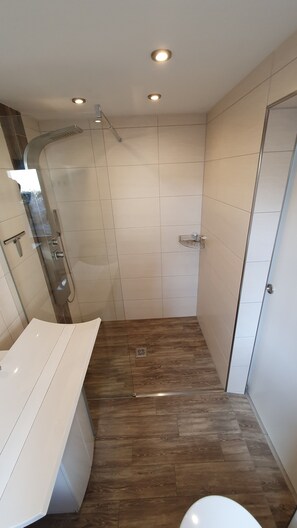 Um banheiro moderno com box de vidro, pia branca e piso de madeira.