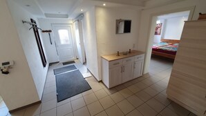 A clean, well-lit room with a wooden cabinet, a small sink, and a bed with a colorful blanket. - Moderne, Top Ausgestattete, Ruhige, Barrierefreie Ferienwohnung (Nonnweiler)