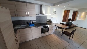A modern kitchen with a built-in oven, a dishwasher, and a dining area with a table and chairs. - Moderne, Top Ausgestattete, Ruhige, Barrierefreie Ferienwohnung (Nonnweiler)