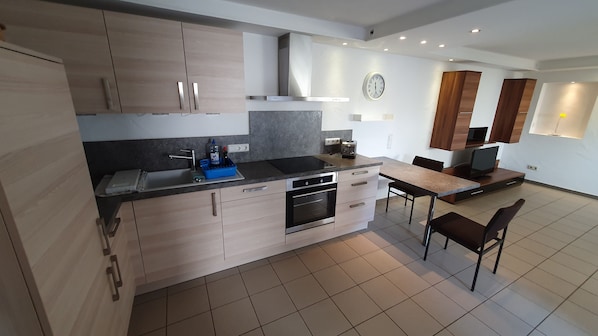 A modern kitchen with a built-in oven, a dishwasher, and a dining area with a table and chairs. - Moderne, Top Ausgestattete, Ruhige, Barrierefreie Ferienwohnung (Nonnweiler)