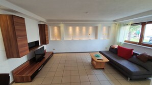 A modern living room with a flat-screen TV, a wooden entertainment unit, a grey sofa with red and brown cushions, a wooden coffee table, and recessed lighting on the ceiling. - Moderne, Top Ausgestattete, Ruhige, Barrierefreie Ferienwohnung (Nonnweiler)