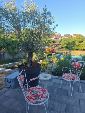 An outdoor seating area with two white metal chairs and a table, surrounded by greenery and a tree. - Moderne, Top Ausgestattete, Ruhige, Barrierefreie Ferienwohnung (Nonnweiler)