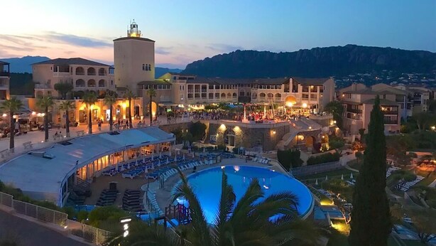 Een resort met een groot zwembad, meerdere gebouwen en een bergachtige achtergrond.