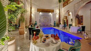 An indoor pool area with a dining setup, surrounded by decorative plants and traditional Moroccan tiles. - Riad Janate & SPA - Chambre Double Standard (Marrakech)
