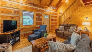 A log cabin interior with a TV, seating area, and wooden walls. - Creekside, Hot Tub, Fire Pit, Fireplace, Quiet, Easy Access (Cosby)