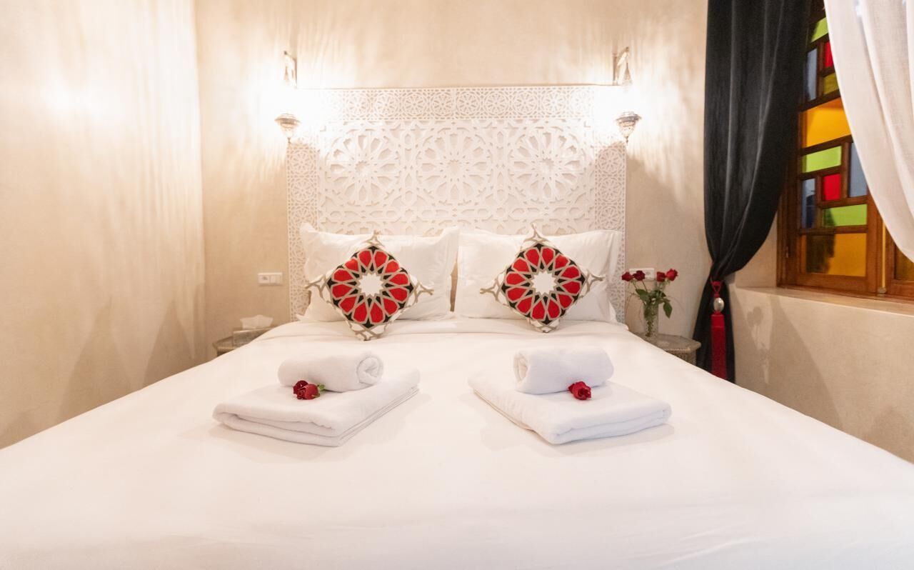 Uma cama bem arrumada com duas almofadas, uma cabeceira decorativa e um vaso com flores.