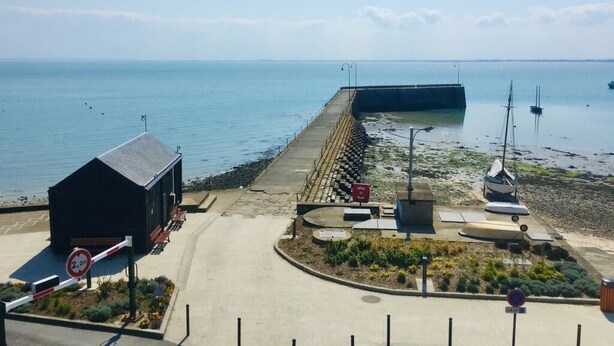 Une jetée côtière avec un petit bâtiment, un bateau et un ciel dégagé.