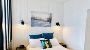 Une chambre à coucher comprenant un lit, deux tables de chevet, une commode, un tableau accroché au mur et deux lampes murales.