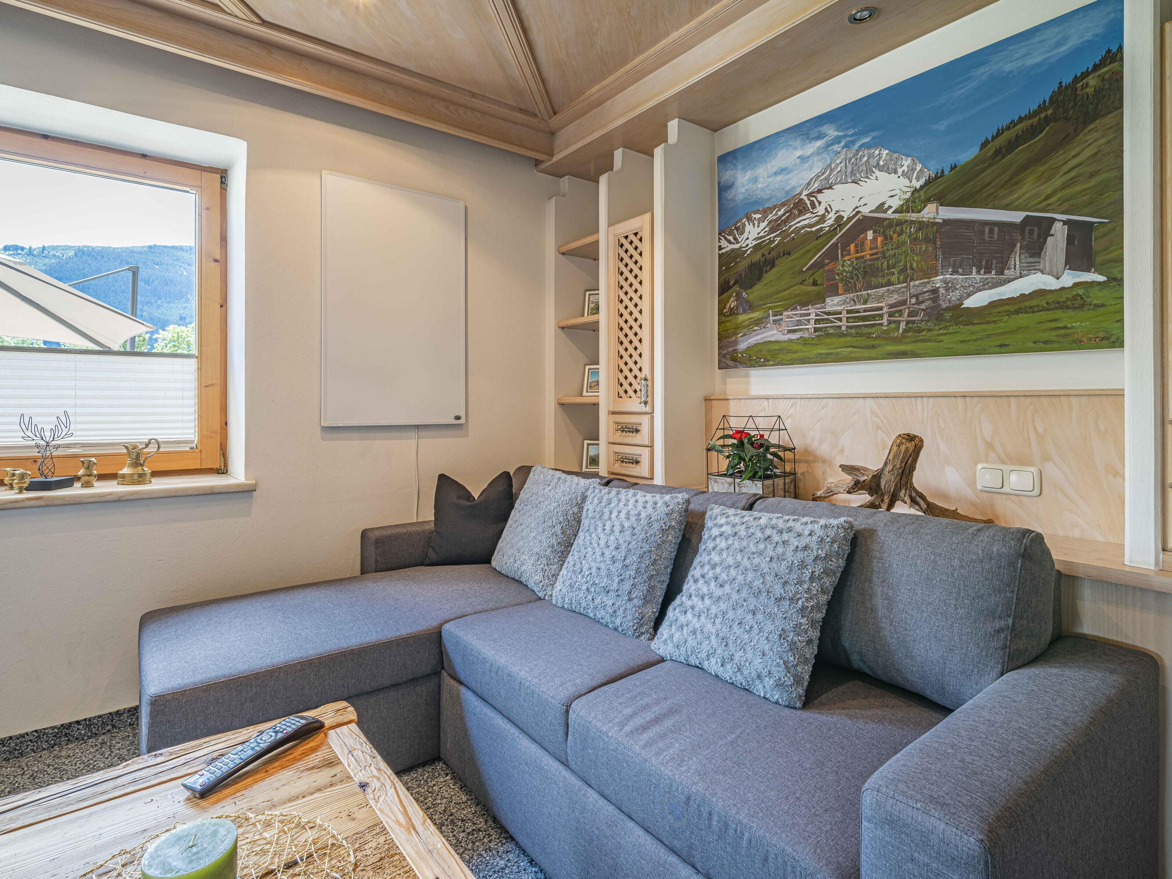 A modern living room with a grey sectional sofa, a wooden coffee table, and a painting of a mountain landscape.