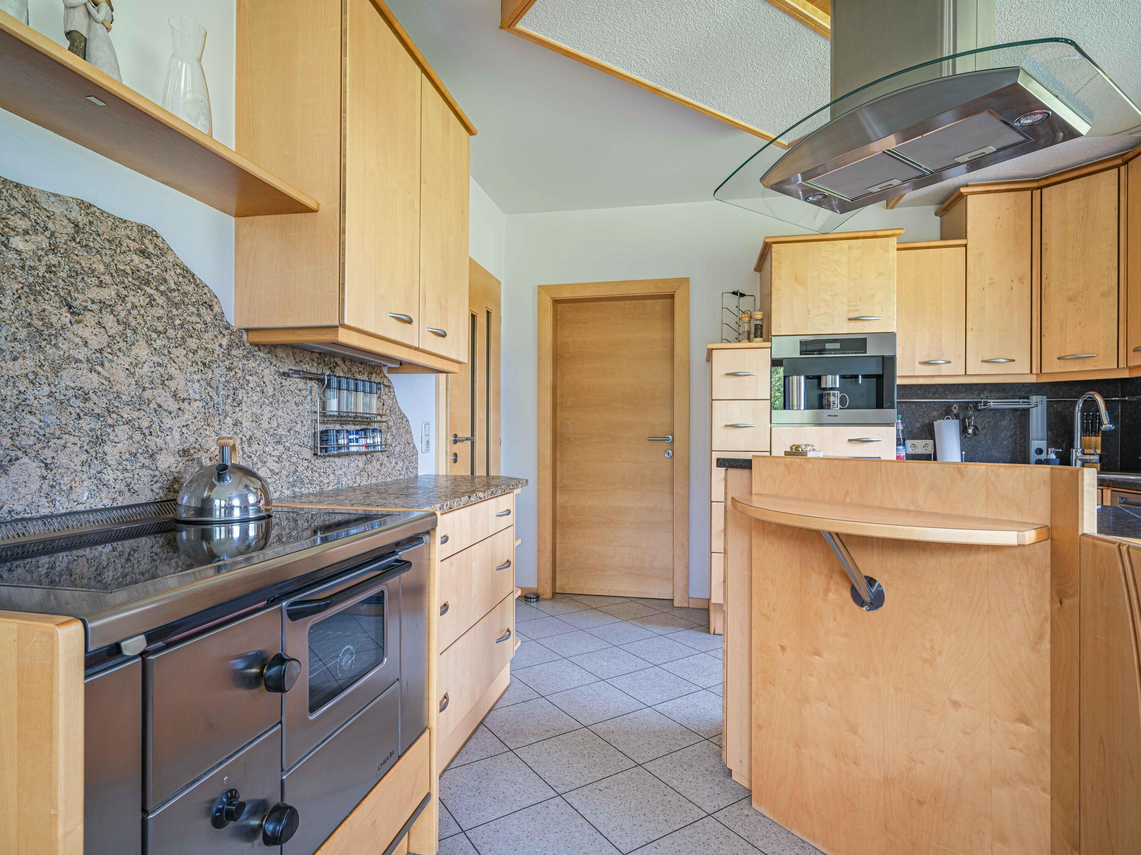 A compact kitchen with wooden cabinets, a built-in oven, and a stainless steel range hood.