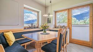 A dining area with a wooden table, dark green upholstered bench seating, and two pendant lights. - Cosy apartment close to Kaprun and Kitzbühel (Stuhlfelden)