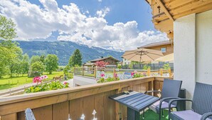 A balcony with wicker furniture, a wooden railing, and a view of mountains and a green landscape. - Cosy apartment close to Kaprun and Kitzbühel (Stuhlfelden)