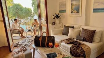 A living room with a sofa, a coffee table with magazines, a glass door leading to a pool area, and a Louis Vuitton bag on the floor.