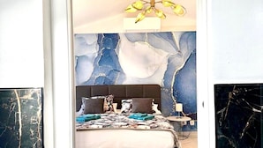 Un dormitorio con cama, mesita de noche, lámpara y una pared con diseño que imita el mármol.