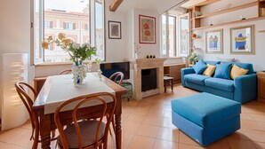 A living room with a dining table, blue sofa, fireplace, and large windows with city views. - TREVI LUXURY PENTHOUSE with panoramic terrace (Roma)