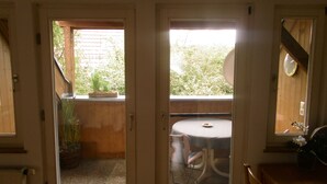 A room with a sliding door leading to a balcony with a table and chairs, a potted plant, and a view of greenery outside. - Apartment in the Schnakenstich, 80 m², 2 bedrooms, living room, eat-in kitchen... (Hochdorf)
