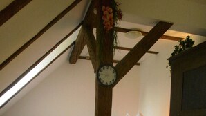 A room with a sloped ceiling, a wooden table, a bed with pillows, and a clock on the wall. - Apartment in the Schnakenstich, 80 m², 2 bedrooms, living room, eat-in kitchen... (Hochdorf)