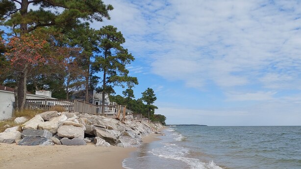 A beach with a wooden fence, large rocks, and a house with a porch. - Private Beach Front Getaway at The Sunshine Beach Cottage. (Scotland)