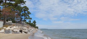 Una spiaggia con una recinzione di legno, grandi rocce e una casa con veranda.