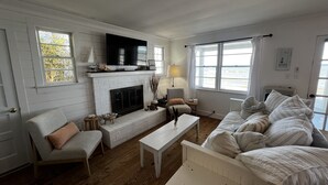 A living room with a fireplace, a television, a sofa, a coffee table, and a view of the outdoors. - Private Beach Front Getaway at The Sunshine Beach Cottage. (Scotland)