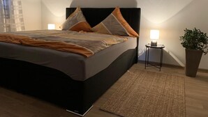 Ein modernes Schlafzimmer mit einem großen Bett, zwei Nachttischlampen, einem kleinen Tisch und einer Topfpflanze.