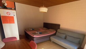 Een knus vertrek met een houten plafond, een bed met hoofdeinde, een bank, een eettafel met stoelen en een koelkast met een berichtje erop.