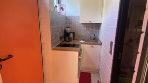 Een kleine keuken met witte kasten, een zwart aanrecht en een rood vloerkleed.