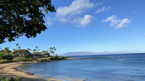Une plage à l’eau d’un bleu cristallin, bordée d’un rivage sablonneux, et d’où l’on peut admirer une chaîne de montagnes au loin.